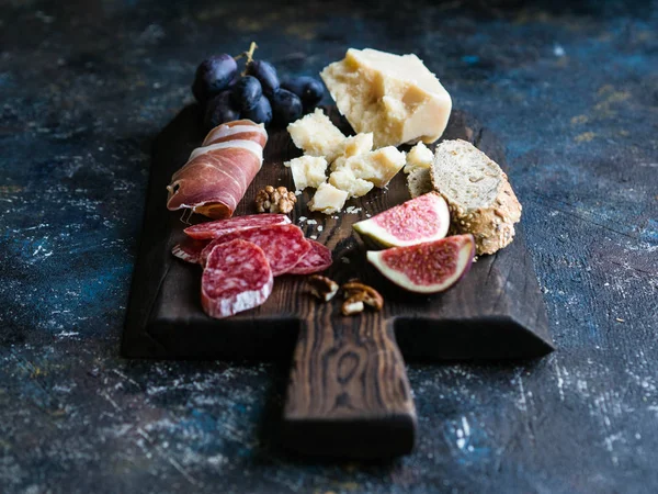 Dark board with various meat, cheese, grapes, bread and figs on a dark background
