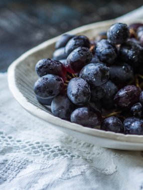 Bir desen karanlık bir arka plan üzerinde beyaz keten peçete üzerinde beyaz bir kase olgun mavi veya mor üzüm demet