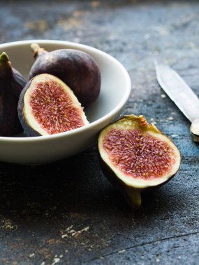 Taze Menekşe bütün incir ve karanlık bir arka plan üzerinde beyaz bir kasede yarım kesilmiş