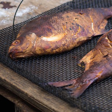 Ahşap bir masa üzerinde bir metal kafes üzerinde iki ev yapımı füme çipura