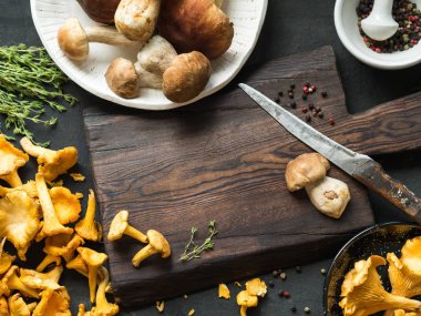 Ham vahşi Cantharellus cibarius mantar ve ham porcini mantar karanlık bir tahta yanında yemek için hazır. Yabani mantar ile kompozisyon. Kopya alanı