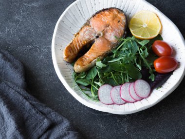 Biftek ile kızarmış somon karışık yeşil salata, domates, turp dilimleri ve limon beyaz plaka üzerinde