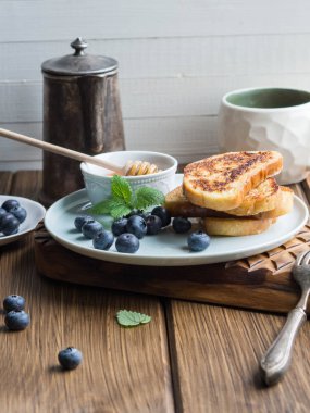 ev yapımı Fransız tostu yığınını yaban mersini ve ahşap doku boyutunda bir tahta üzerinde mavi bir tabakta bal ile serpilir. lezzetli kahvaltı.