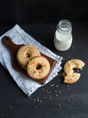Tanımlama bilgileri halka yığını fıstık bir ahşap tahta üzerinde serpilir. Bir cam şişe süt yakındır. Üstten Görünüm. Koyu arka plan