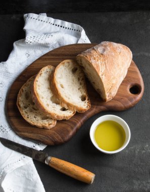 ekmek dilimleri ahşap tahta üzerinde koyu arka plan üzerinde beyaz kase zeytinyağı ile kesilmiş