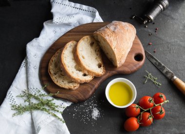 ekmek dilimleri ahşap tahta üzerinde beyaz kase, tuz, zeytin yağı ile domates ve kekik koyu arka plan üzerinde kesti. Üstten Görünüm