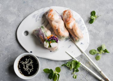 Havuç, kırmızı lahana, Mısır marul ve beyaz seramik tahta üzerinde karides böreği. Soya soslu susam gri bir arka plan üzerinde