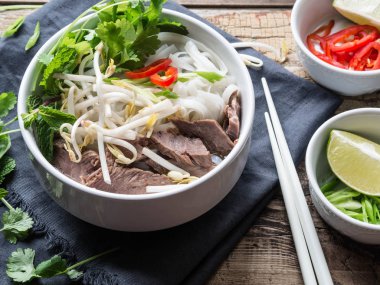Geleneksel Vietnam çorba-pho sığır eti ve pirinç noodle, nane ve Salantro, yeşil soğan, biber, fasulye filizi ve kireç ahşap tahta arka plan üzerinde beyaz bir kase. Asya gıda. Üstten Görünüm