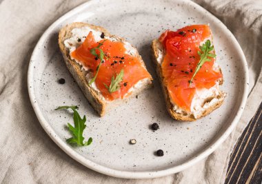 Gri bir keten havlu üzerinde beyaz bir plaka üzerinde füme somon ve krem peynir ile iki tost