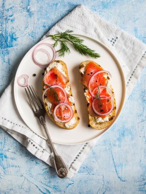 İki sandviç mavi zemin üzerine beyaz plaka üzerinde füme somon ve krem peynir ile. Üstten Görünüm