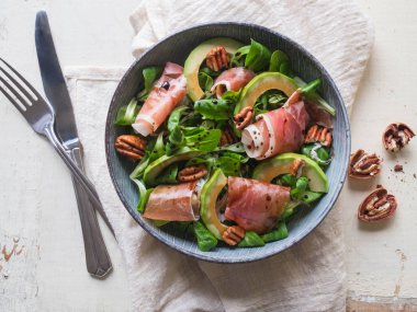 Beyaz ahşap bir masa karanlık bir peçeteye jambon, avokado ve pekan fındık ile mısır salatası. Üstten Görünüm