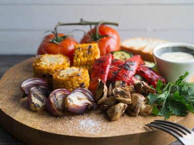 Yuvarlak bir tahta üzerinde çeşitli ızgara sebze. Domates, kabak, soğan, Mısır, mantar, kırmızı biber