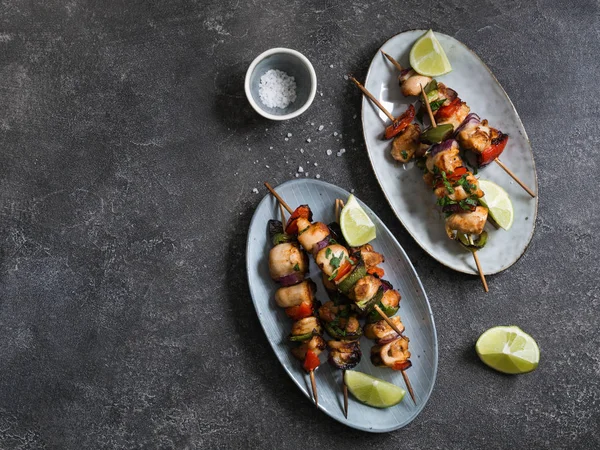 Chicken on skewers on oval dish and fresh salad plate with mixed greens with chicken on skewers on grey background