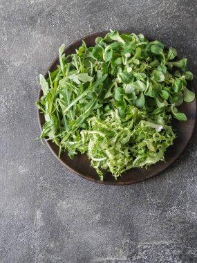 Yeşil salata, çeşitli gri bir arka plan üzerinde ahşap tabak içinde bırakır. Küçük taş marul, Mısır marul, friz, roka. 