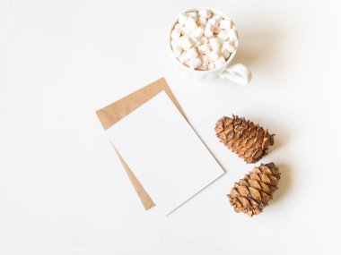 Sıcak içecek ve kremalı beyaz bardak, mektup için kağıt kart, zarf ve beyaz arka planda iki sedir konisi. Üst Manzara. Boşluğu kopyala