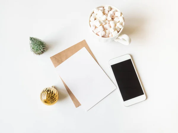ホットドリンクとマシュマロ付きの白いマグカップ、手紙用の紙カード、封筒、白い電話と白い背景にクリスマスの装飾。最上階だスペースのコピー — ストック写真