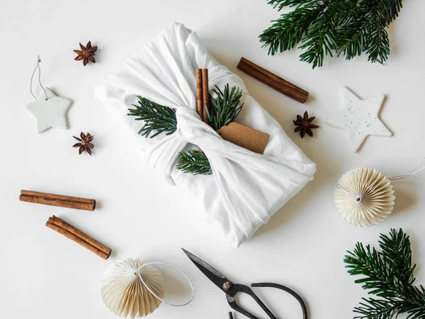 Flach liegendes Weihnachtsgeschenk in Stoff gewickelt mit Papieranhänger, Tannenzweig und Zimt. wiederverwendbare nachhaltige Geschenkverpackung Alternative. Ansicht von oben. — Stockfoto