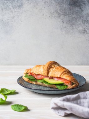 Somon dilimli Fransız kruvasanı, ahşap arka planda mavi tabakta avokado ve ıspanak. Boşluğu kopyala