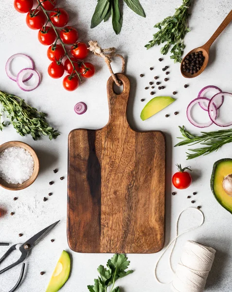 Fresh raw greens, vegetables, spices and kitchen were frame and cutting board in the center on grey background. top view, — Stock Photo, Image