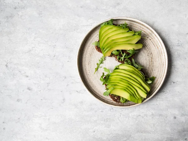 Tostadas caseras saludables con rúcula y aguacate sobre pan de grano de centeno en plato sobre fondo gris. Vista superior. Copiar espacio —  Fotos de Stock