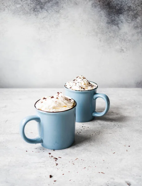 Two blue mugs with hot chocolate, whipped cream, chocolate chips on a gray background. Copy space