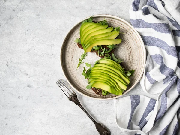 Tostadas caseras saludables con rúcula y aguacate sobre pan de grano de centeno en plato sobre fondo gris. Vista superior . — Foto de Stock