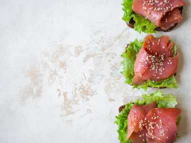 Somon dilimli çavdar ekmeği tostu, susam ve gri arka planda marul. Üst Manzara. Boşluğu kopyala