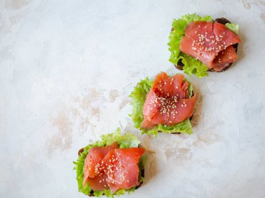 Somon dilimli çavdar ekmeği tostu, susam ve gri arka planda marul. Üst Manzara. Boşluğu kopyala