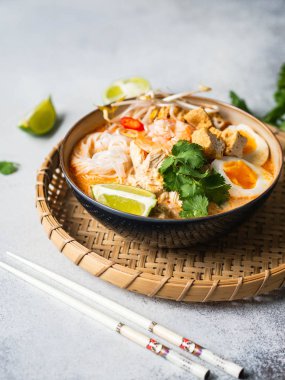 Malezya eriştesi laksa çorbası tavuk, karides ve tofu ile gri arka planda bir kasede