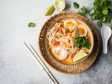 Malezya eriştesi laksa çorbası tavuk, karides ve tofu ile gri arka planda bir kasede