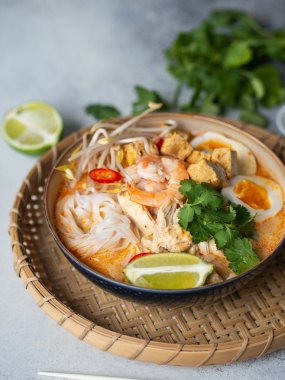 Malezya eriştesi laksa çorbası tavuk, karides ve tofu ile gri arka planda bir kasede