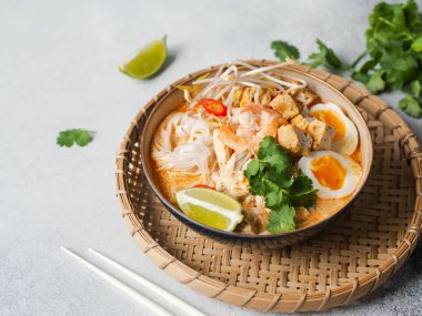 Malezya eriştesi laksa çorbası tavuk, karides ve tofu ile gri arka planda bir kasede. Boşluğu kopyala