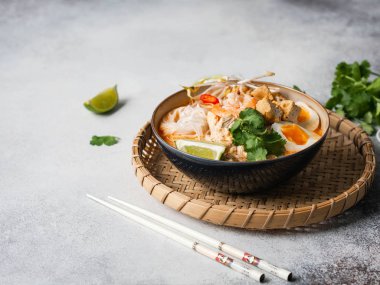 Malezya eriştesi laksa çorbası tavuk, karides ve tofu ile gri arka planda bir kasede