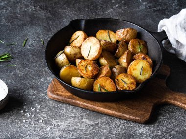 Siyah dökme demir tavada kızarmış patates ve koyu gri arka planda otlar.