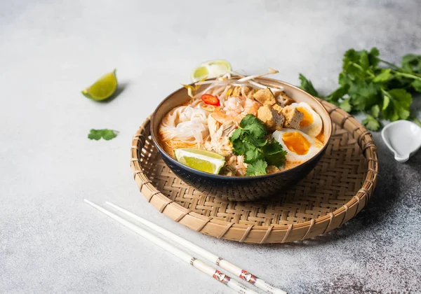 Zuppa di noodles malesi con pollo, gamberetti e tofu in una ciotola su sfondo grigio. Copia spazio — Foto Stock