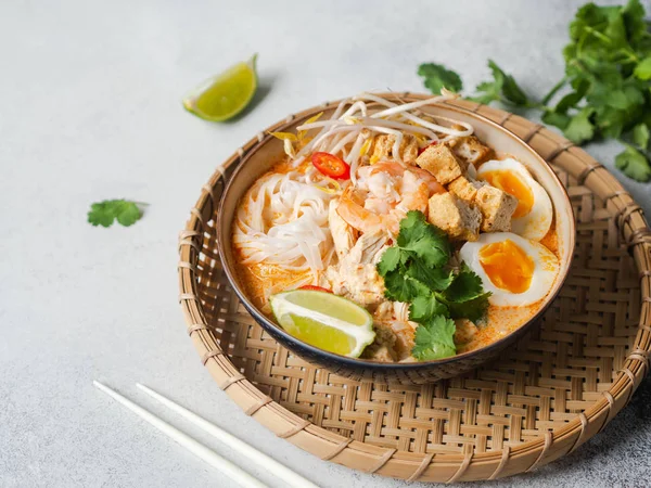 Zuppa di noodles malesi con pollo, gamberetti e tofu in una ciotola su sfondo grigio. Copia spazio — Foto Stock