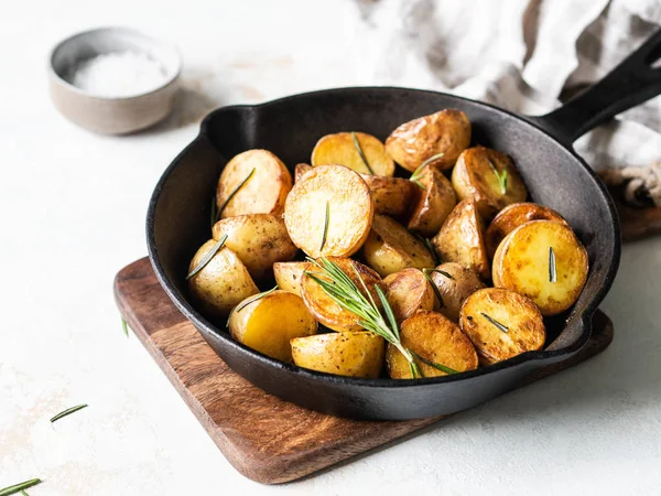 Sartén de hierro fundido negro con cuñas de patata asadas fritas con hierbas sobre un fondo claro — Foto de Stock