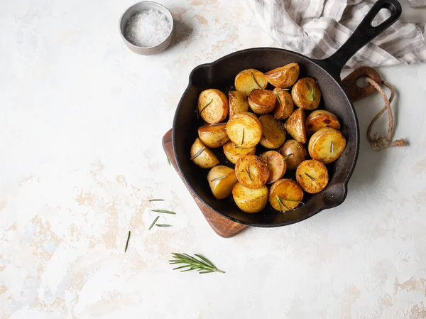 Sartén de hierro fundido negro con cuñas de patata asadas fritas con hierbas sobre un fondo claro . —  Fotos de Stock