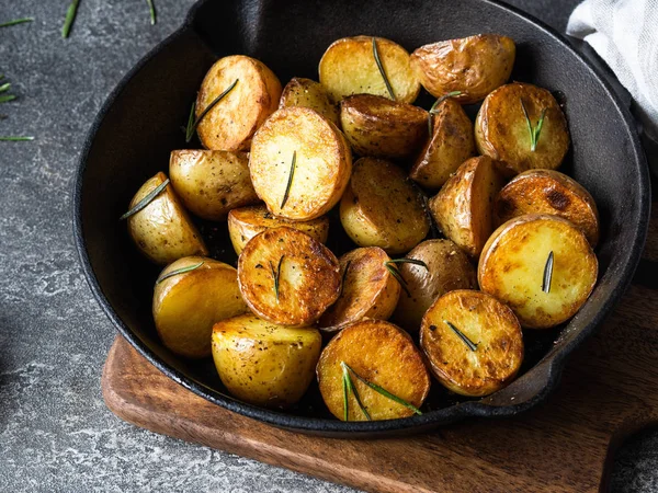 Sartén de hierro fundido negro con cuñas de patata asadas fritas con hierbas sobre fondo gris oscuro — Foto de Stock