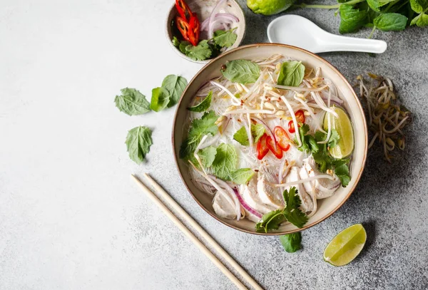 Zuppa tradizionale vietnamita-pho ga in ciotola con pollo e riso tagliatelle, menta e coriandolo, cipolla rossa, peperoncino, germogli di fagioli e lime su fondo grigio. Cibo asiatico. Ricevuto. Vista dall'alto — Foto Stock