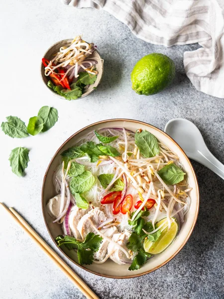 Sopa vietnamita tradicional-pho ga em tigela com macarrão de frango e arroz, hortelã e coentro, cebola vermelha, pimenta, brotos de feijão e limão em fundo cinza. Comida asiática. Espaço para cópia. Vista superior — Fotografia de Stock