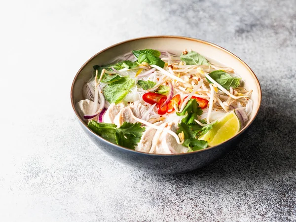 Традиционный вьетнамский суп-фо га в миске с курицей и рисовой лапшой, мятой и кинзой, красным луком, чили, фасолью и лаймом на сером фоне. Азиатская еда. Копирование пространства . — стоковое фото