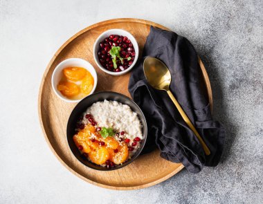 Taze mandalina dilimleri ve nar tohumlarıyla yulaf ezmesi, badem ezmesi ve ahşap tepside siyah bir kasede nane şekeri. Üst görünüm