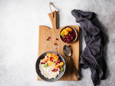 Taze mandalina dilimleri ve nar tohumlarıyla yulaf ezmesi, badem ezmesi ve ahşap tahtadaki mavi bir kasede naneli şeker. Boşluğu kopyala.