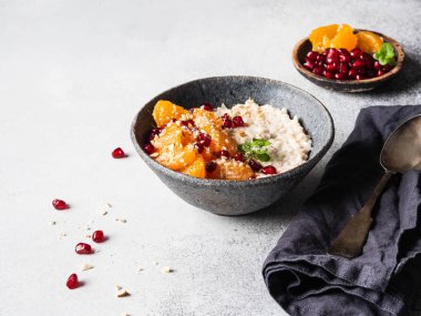 Taze mandalina dilimleri ve nar tohumlarıyla yulaf ezmesi, badem ezmesi ve gri arka planda mavi bir kasede naneli şeker. Boşluğu kopyala