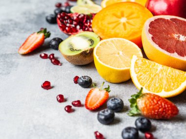 Hurma, yaban mersini, portakal, kivi, çilek, greyfurt, nar ve portakal dilimleriyle renklendirilmiş mevsimsel sağlıklı meyve kompozisyonu. Boşluğu kopyala