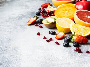 Hurma, yaban mersini, portakal, kivi, çilek, greyfurt, nar ve portakal dilimleriyle renklendirilmiş mevsimsel sağlıklı meyve kompozisyonu. Boşluğu kopyala