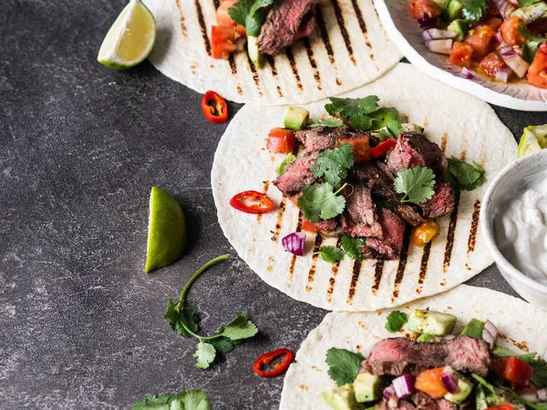 Tortillas with vegetables and beef steak slices. Avocados, tomatoes, red onions and meet with cilantro and lime juice in tortillas. Mexican food. Copy space