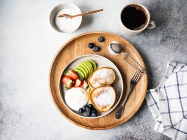 Lezzetli kahvaltı, börek, krep, pudra şekeri, meyve ve böğürtlen ve tabakta ekşi krema ve ahşap tepside bir fincan kahve. Üst görünüm
