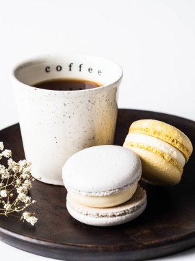 Beyaz seramik fincanlı iki pastel badem kurabiyesi. Ahşap tabakta, beyaz arka planda.